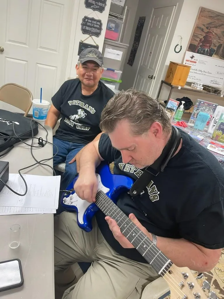 Two veterans playing electric guitars together in the clubhouse