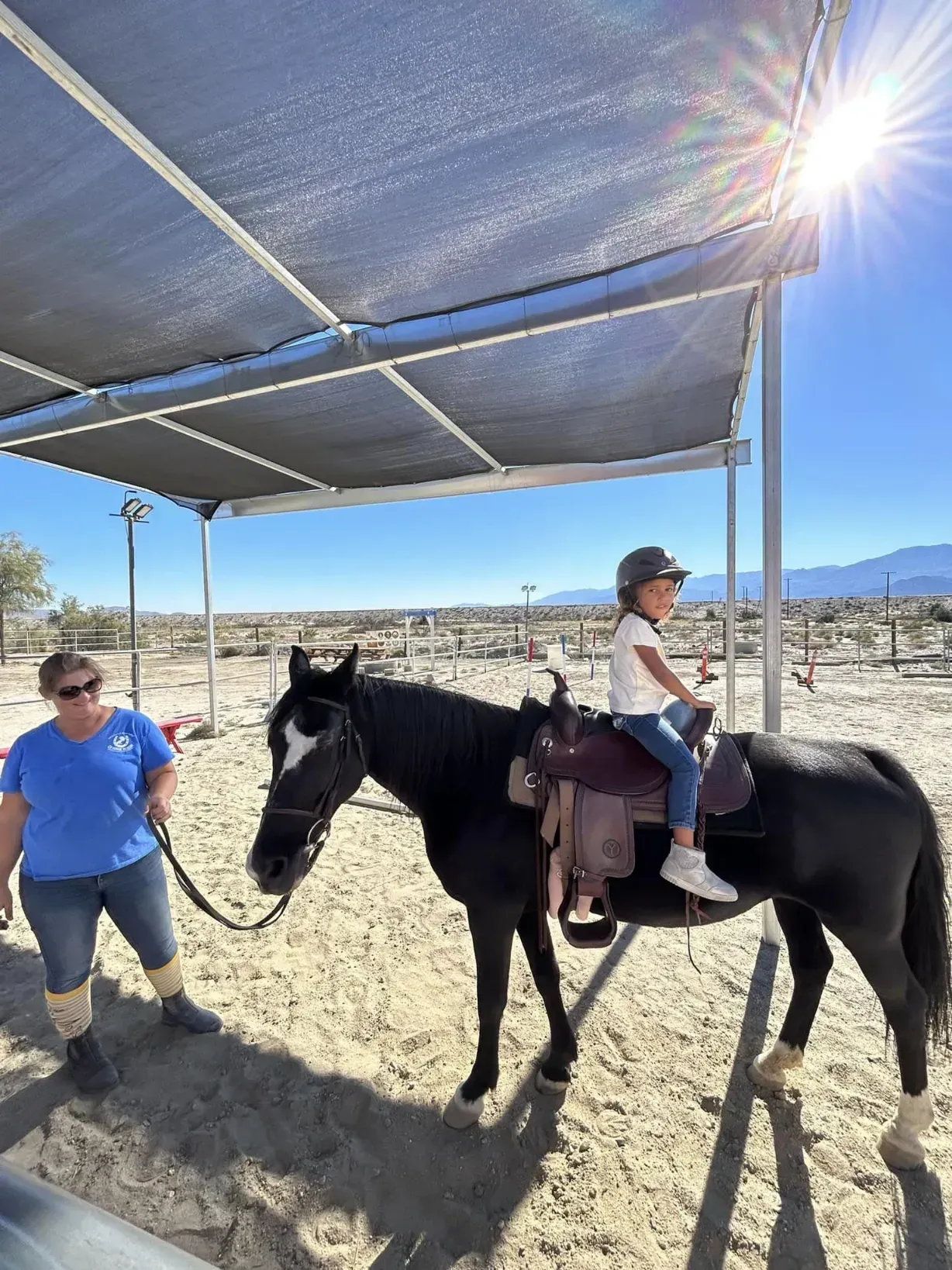 A child on horseback being led by a volunteer during a riding lesson